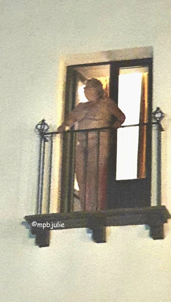It's an over exposed and grainy photo of me naked on a small balcony. I'm holding the railings and looking to my right.The room behind is lit.