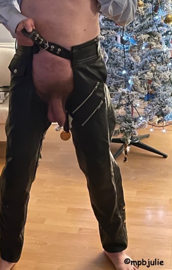 Master standing in front of the Christmas tree wearing a pair of leather chaps and nothing else. You can see his cock