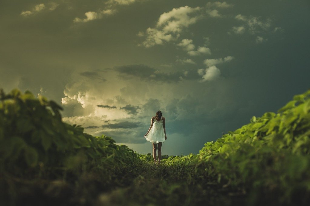 A girl stands between two hills, she seems to be close to the sky