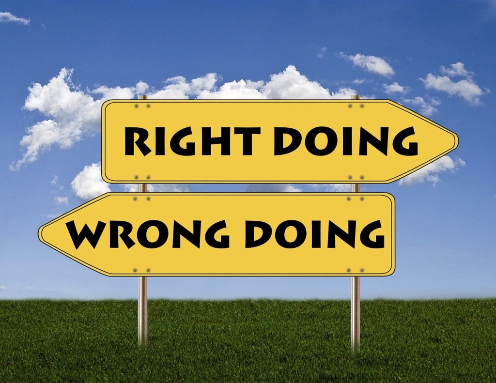 Sign post saying right doing wrong doing against the back drop of a blue sky and grass