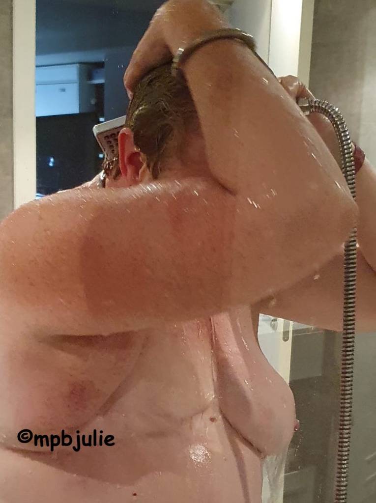 Me in the shower. I'm holding the shower attachment and washing the back of my hair and neck. My right arm shields my face. My mastectomy scar is evident and on the other side may remaining boob. 