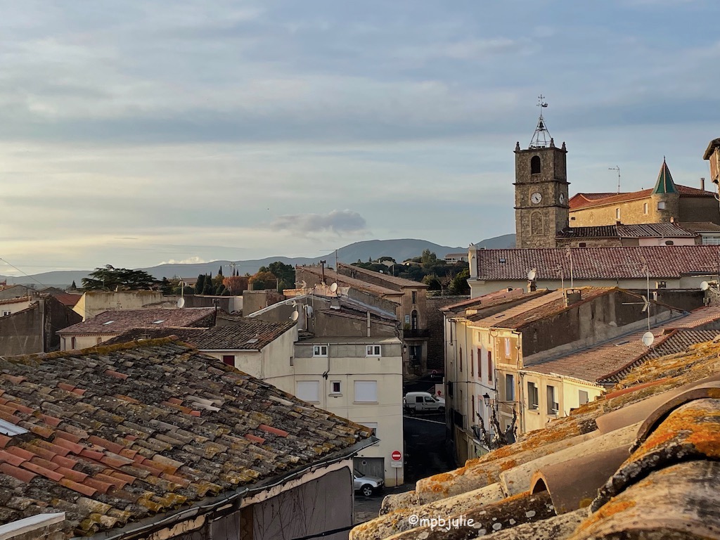 This image is of a small town in the south of France from our roof terrace. You can see a clock tower and a chateau type building and lots of roof tops. Then hills in the distance. It's cloudy but it was taken in December. 