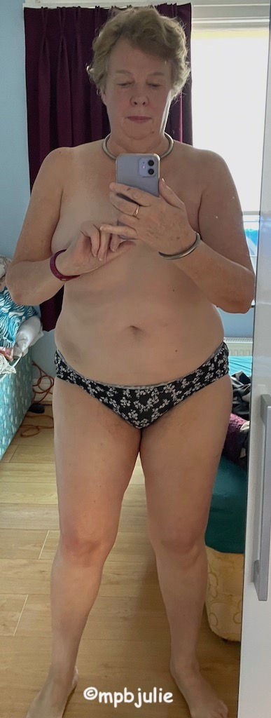 I am standing in front of a mirror facing the front. I'm wearing black and white knickers. There is an unmade bed and a bit of clutter behind.