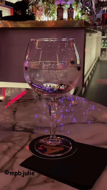 A gin and tonic sitting on a table with a hotel bar in the background.