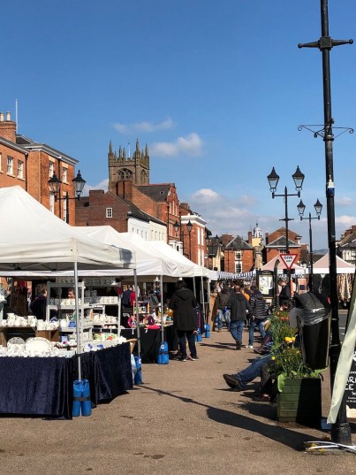 A sunny day, blue sky. Building including a church in the background. In the foreground market stalls.
