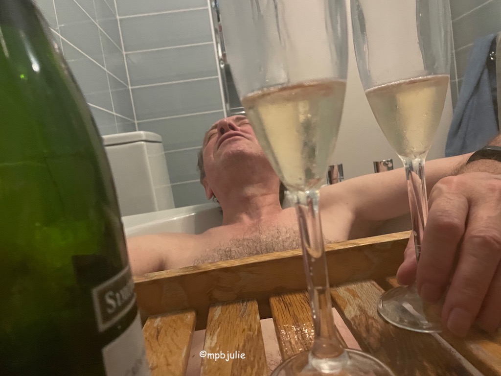 Master is lying back in the bath, his hand on one of two champagne glasses. The bottle is to the left on a shelf across the bath. You can't see much of him, head, shoulders and chest. But he is laying back relaxed. 