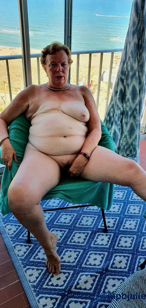 I'm sitting naked on a chair in an enclosed balcony. There is a beach view behind me.