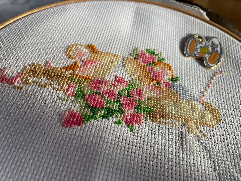 Cross stitch of two mice kissing. She is wearing a flower head dress and there are flowers between them. It's not finished. 