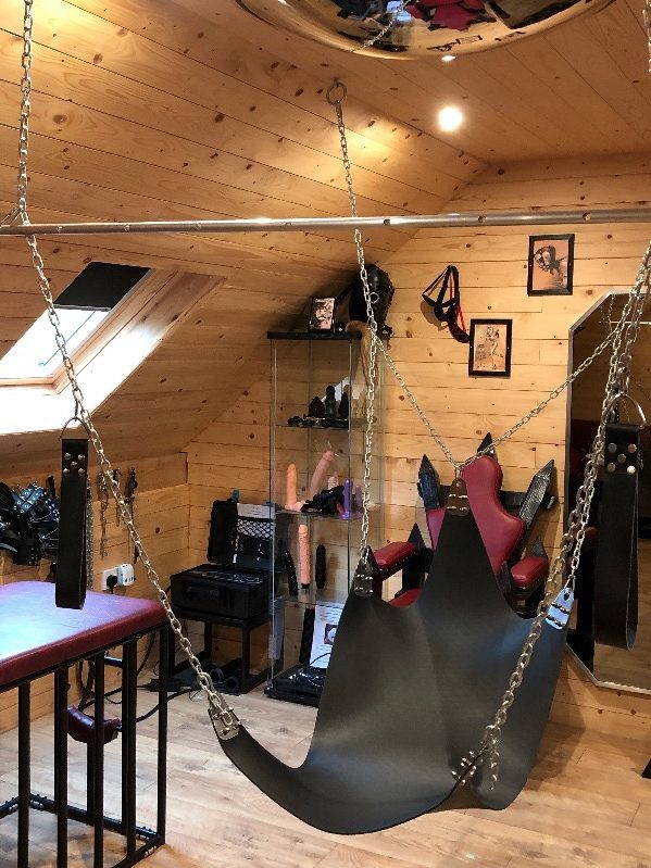 A swing, set within a BDSM dungeon room.