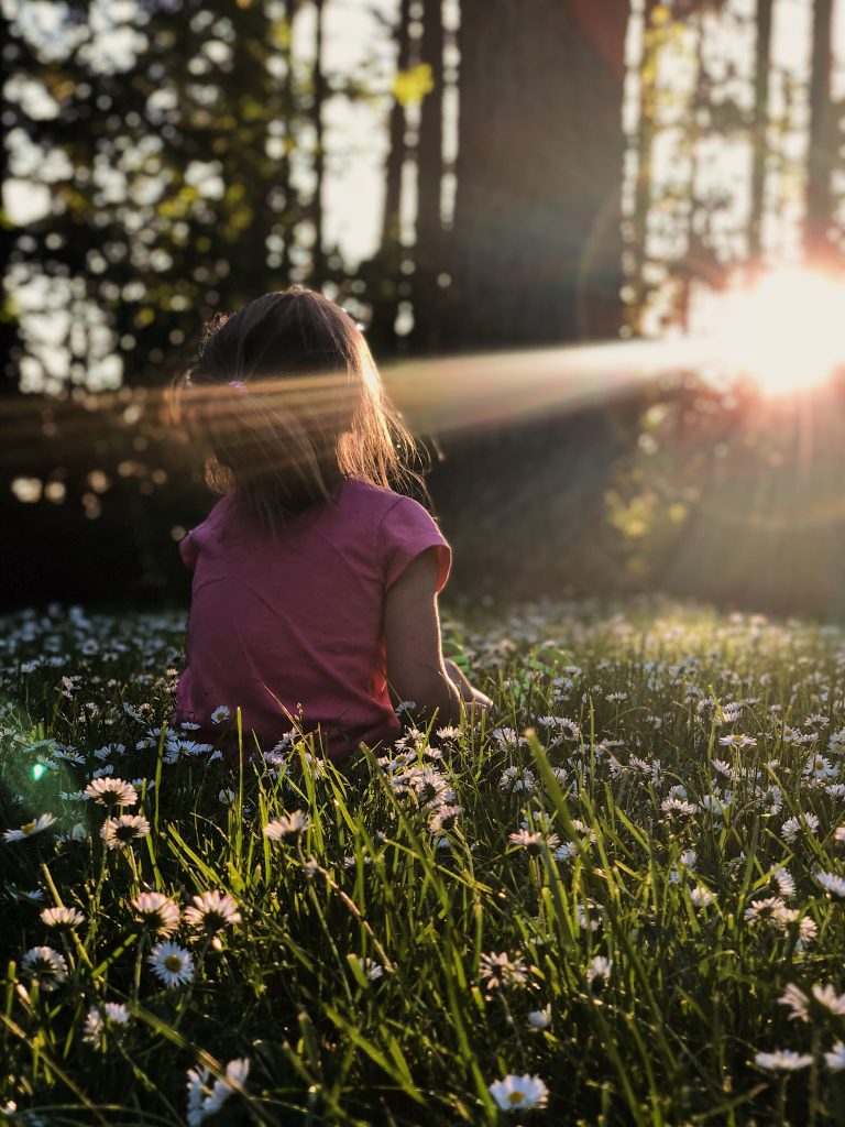 A girl standing in s field of daisies day dreaming into the sun.