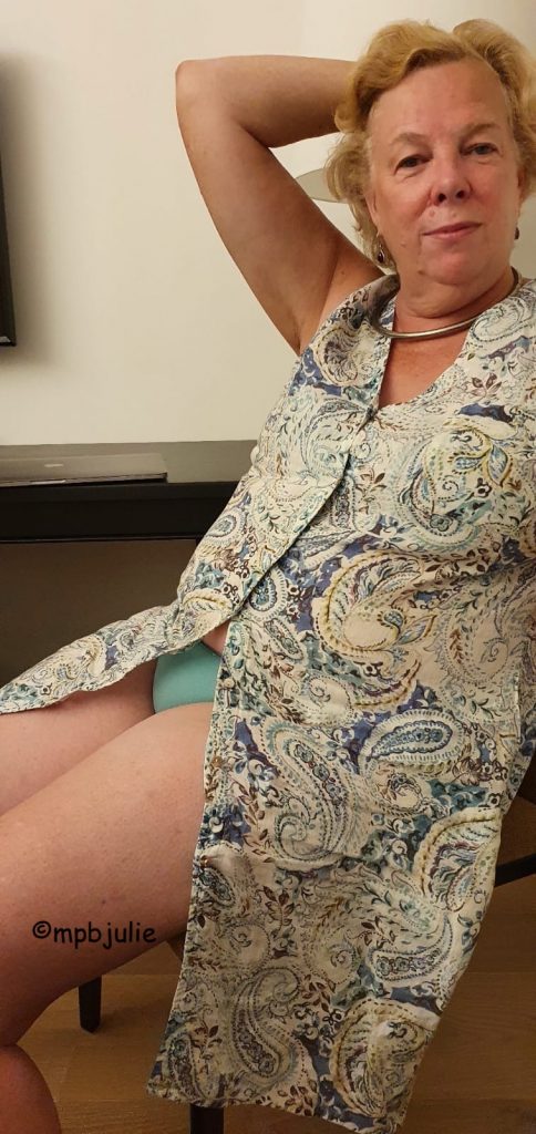 Me lounging back in a chair wearing a summer dress split at the waist. I'm wearing light blue knickers.