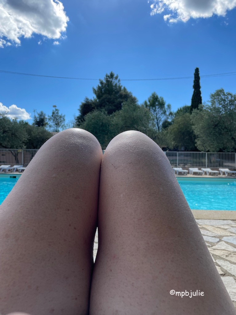 I'm lying on a subbed by a pool. You can see my knees and a bit of my legs the pool, sunbeds, trees and the sky. A couple of fluffy clouds float by.